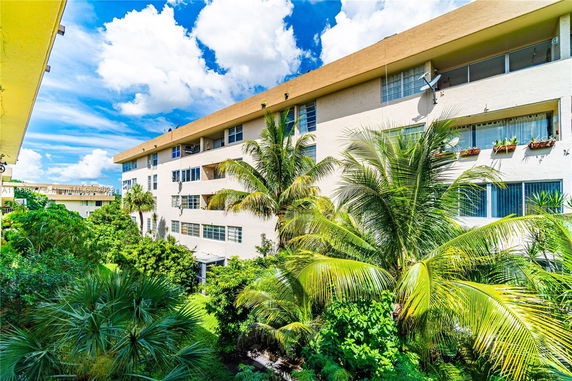 View of a multi-story building with plants and trees in front.