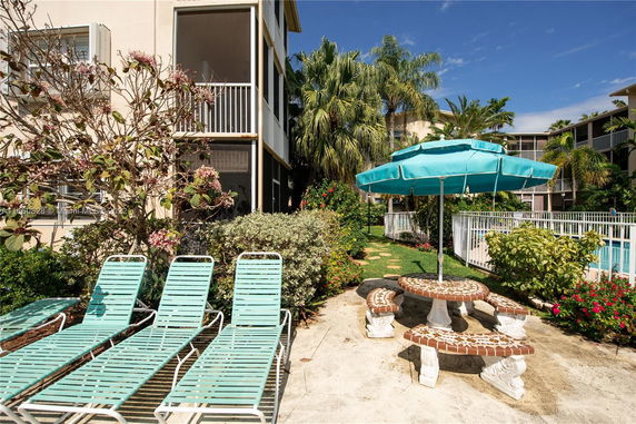 Outdoor area with lounge chairs, a table with an umbrella, and a view of a swimming pool.