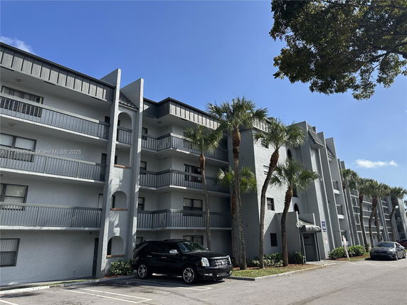 Front view of a multi-story residential building with balconies and palm trees.