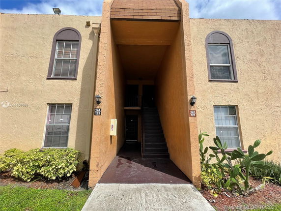 Front view of a two-story apartment building with arched windows and an entryway staircase.