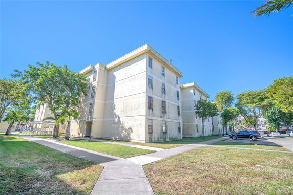 Front view of a multi-story residential building with walkways and parking area.