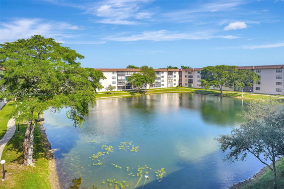 A multi-story apartment building with a pond and trees in the foreground.