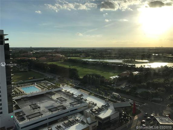 Panoramic view from a high-rise building, overlooking a rooftop with pools and the surrounding landscape.