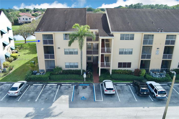Front view of a multi-story apartment building with balconies and parking spaces.