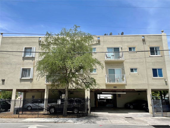Front view of a three-story residential building with balconies and a gated parking area at the ground level.