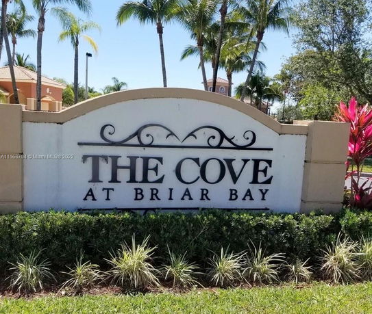 Front view of the entrance sign for 'The Cove at Briar Bay' with palm trees in the background.