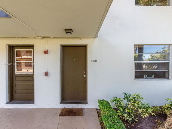 Front entrance of a residential building unit with a brown door and adjacent window.