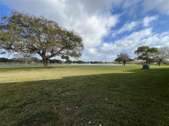 Open grassy area with large trees and a distant view of a body of water.