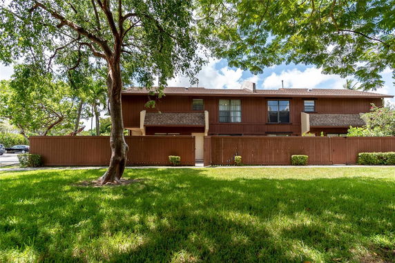 Front view of a two-story wooden townhouse with a fenced yard.