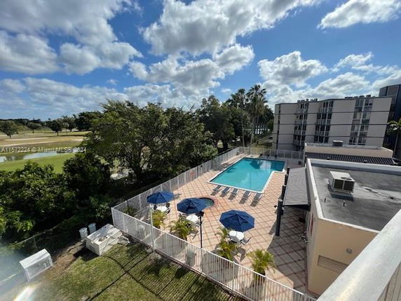 Aerial view of a swimming pool area with blue umbrellas and lounge chairs next to a building.