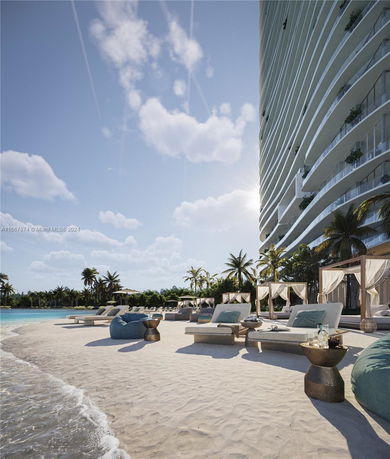 Side view of a modern multi-story building next to a beach with lounge chairs and cabanas.