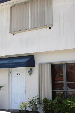 Front view of a building entrance with a blue awning and shuttered windows.