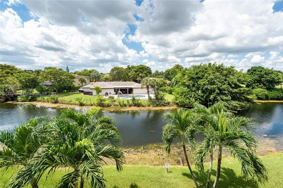 View of a house with a swimming pool near a water body and lush greenery.
