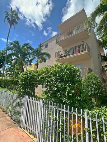 Side view of a multi-story residential building with balconies and a surrounding fence.