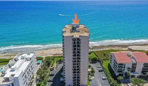 Aerial view of a tall beachfront building with a rooftop containing equipment, overlooking the ocean.
