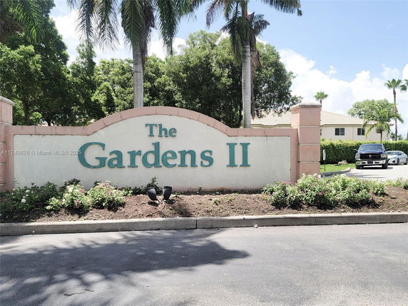 Front view of residential area entrance with a sign reading 'The Gardens II'.