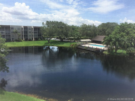 View of a pond with a swimming pool and mid-rise buildings in the background.