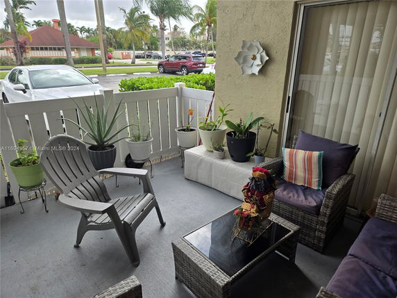 Outdoor patio with furniture and potted plants overlooking a parking area and street.