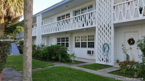 Front view of a two-story building with decorative balcony railings and a garden.
