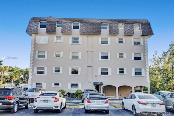 Front view of a multi-story residential building with arched entrances and parking area.