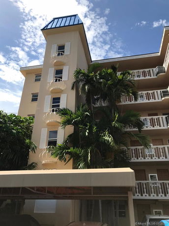 Front view of a multi-story building with balconies and palm trees.