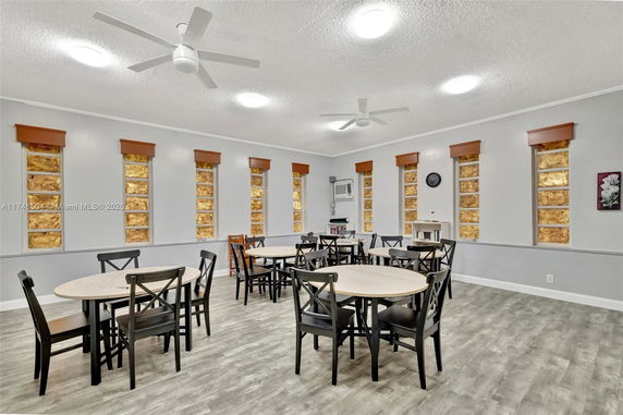 Room with tables and chairs arranged for recreational activities, featuring multiple small windows and ceiling fans.