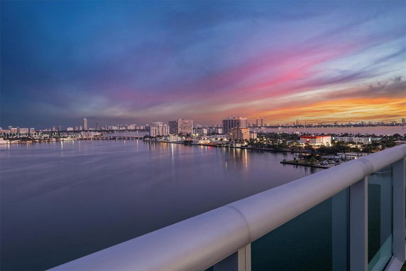 Scenic view of a city skyline and water from a balcony at sunset.