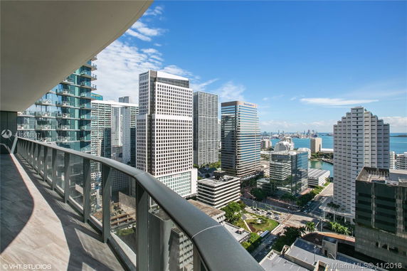 View from a high-rise balcony overlooking multiple skyscrapers and a distant body of water.