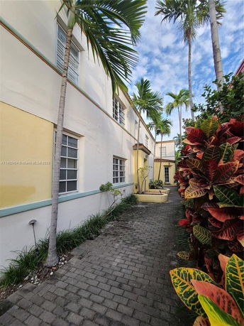 Side view of a multi-story building with windows and a walkway lined with plants.