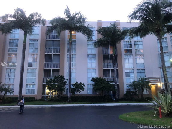 Front view of a multi-story building with large windows and balconies, surrounded by palm trees.