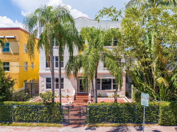 Front view of a multi-story house with palm trees and a fence.