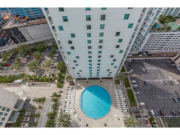 Aerial view of a tall building with a circular swimming pool and adjacent outdoor parking area.