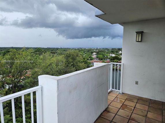 View from a balcony overlooking a vast green landscape with buildings in the distance under cloudy skies.