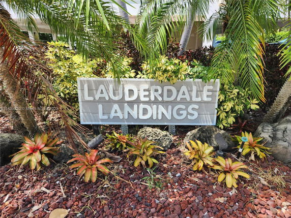 Sign reading 'Lauderdale Landings' surrounded by tropical plants.