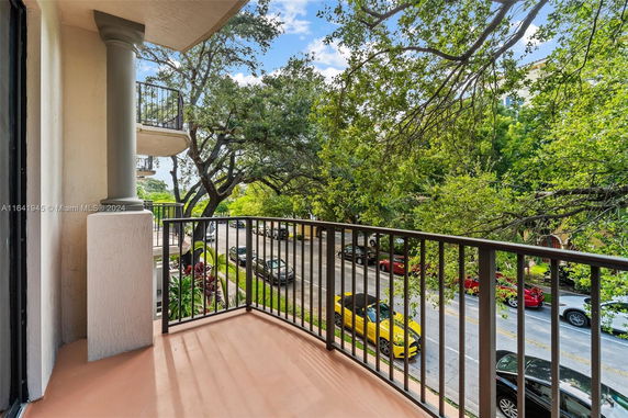 Balcony view overlooking a street lined with trees and parked cars.