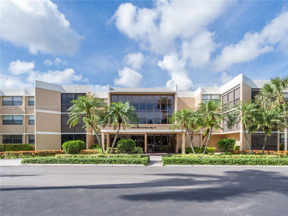 Front view of a modern three-story building with large windows and palm trees in front.