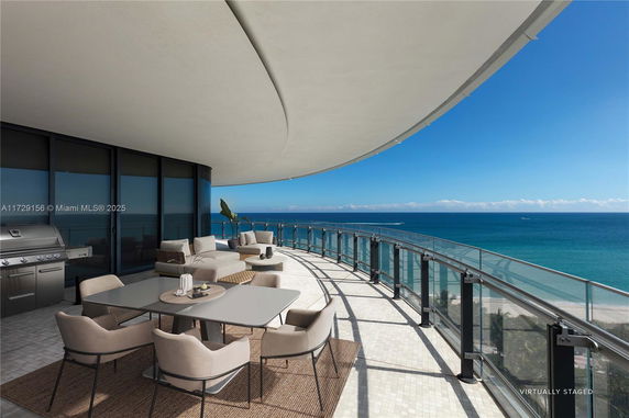 Panoramic view from a balcony overlooking the ocean with outdoor seating and dining area.