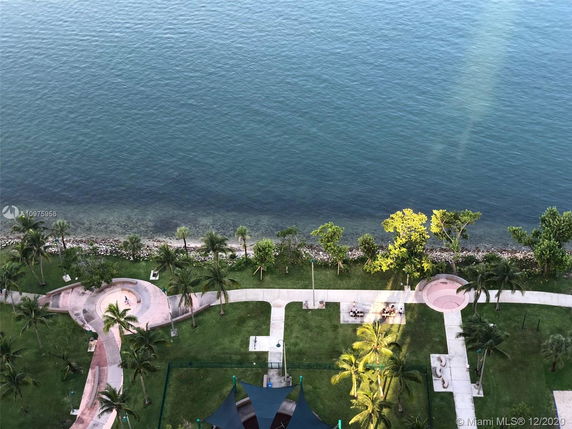 Aerial view of a coastal area with walking paths, palm trees, and a shoreline.