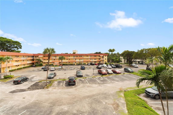 Outdoor parking area with multiple cars in front of a multi-story residential building.