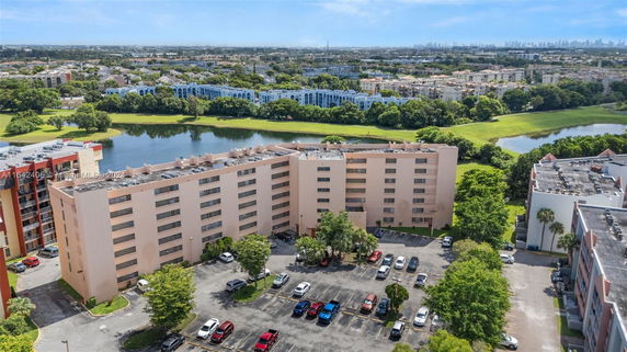 Aerial view of a mid-rise residential building with parking area and green surroundings.