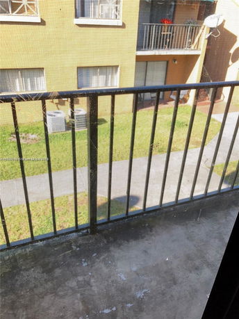 View from a balcony or window showing a building with windows and a grassy area below.
