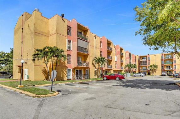 Front view of a multi-story apartment building with balconies and a parking area.
