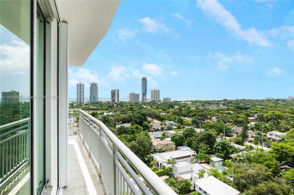Panoramic view of a cityscape with tall buildings in the distance and a balcony railing in the foreground.