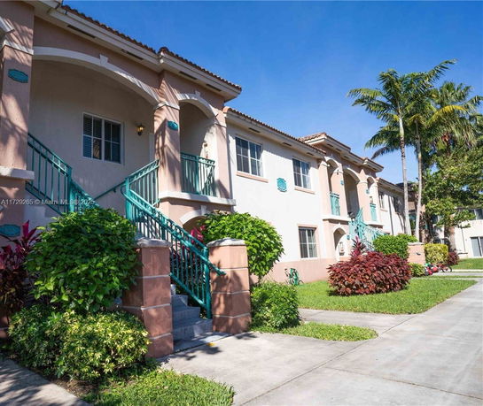 Front view of a two-story residential building with an outer staircase and decorative plants.