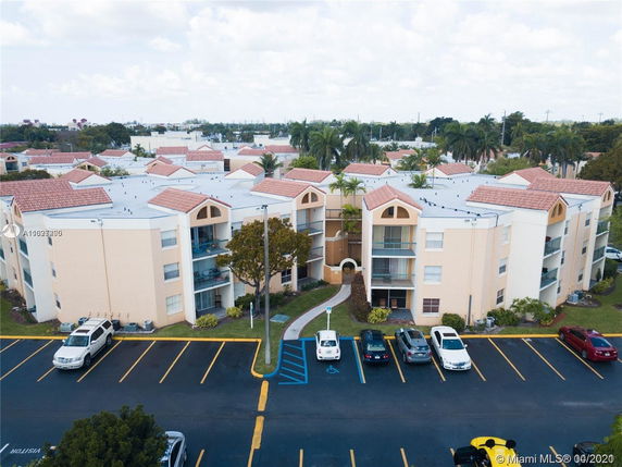 Front view of a multi-story apartment building with balconies and parked cars.