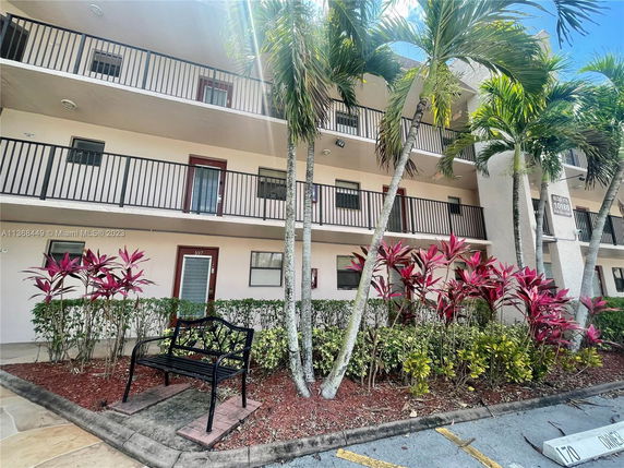 Front view of a multi-story building with balconies and surrounding plants.