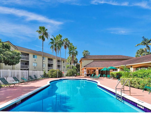 Outdoor swimming pool area with surrounding buildings and palm trees.