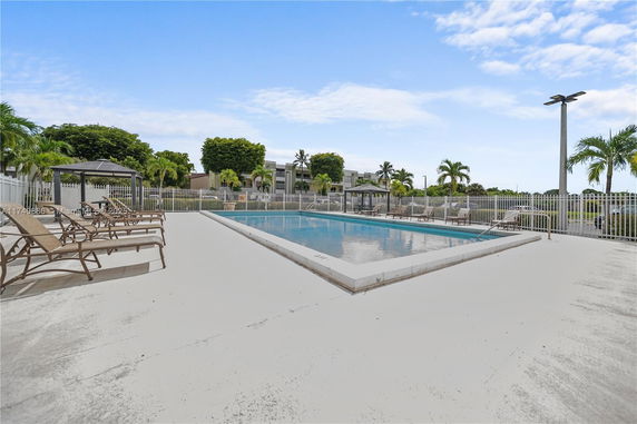 Outdoor swimming pool area with loungers and surrounding fence.