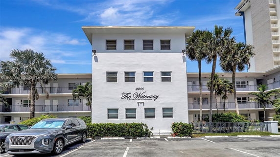 Front view of a multi-story condominium building with balconies and palm trees.