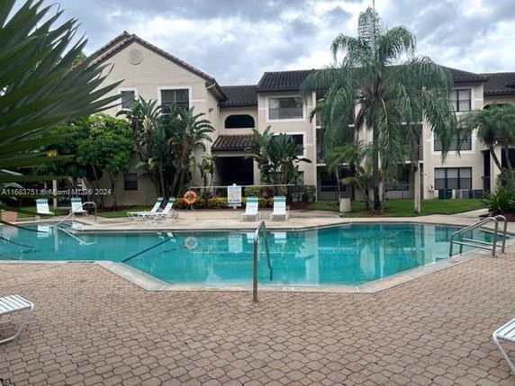 View of a residential building with an outdoor swimming pool surrounded by palm trees and lounge chairs.